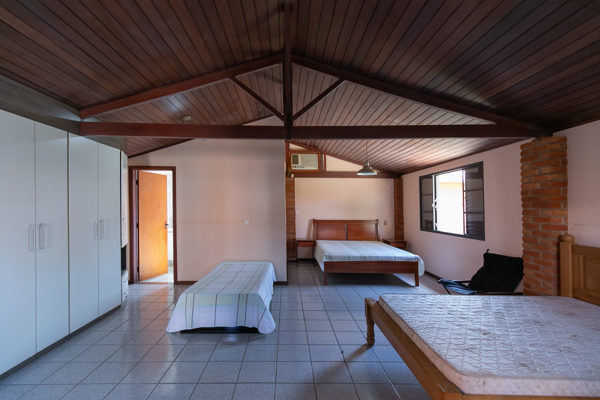Suíte ampla da casa anexa com teto de madeira e várias camas