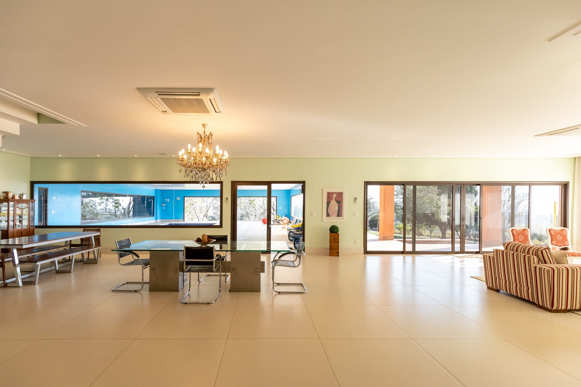 Salão amplo com mesa de jantar, lustre e janela para a piscina interna