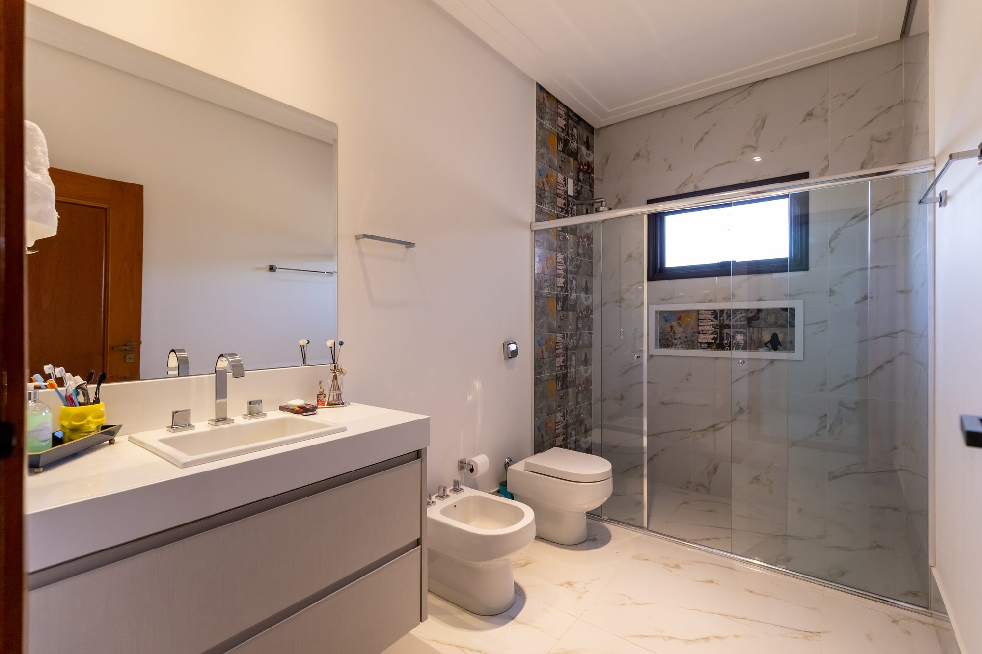 Banheiro amplo em mármore com box de vidro e faixa de azulejos coloridos