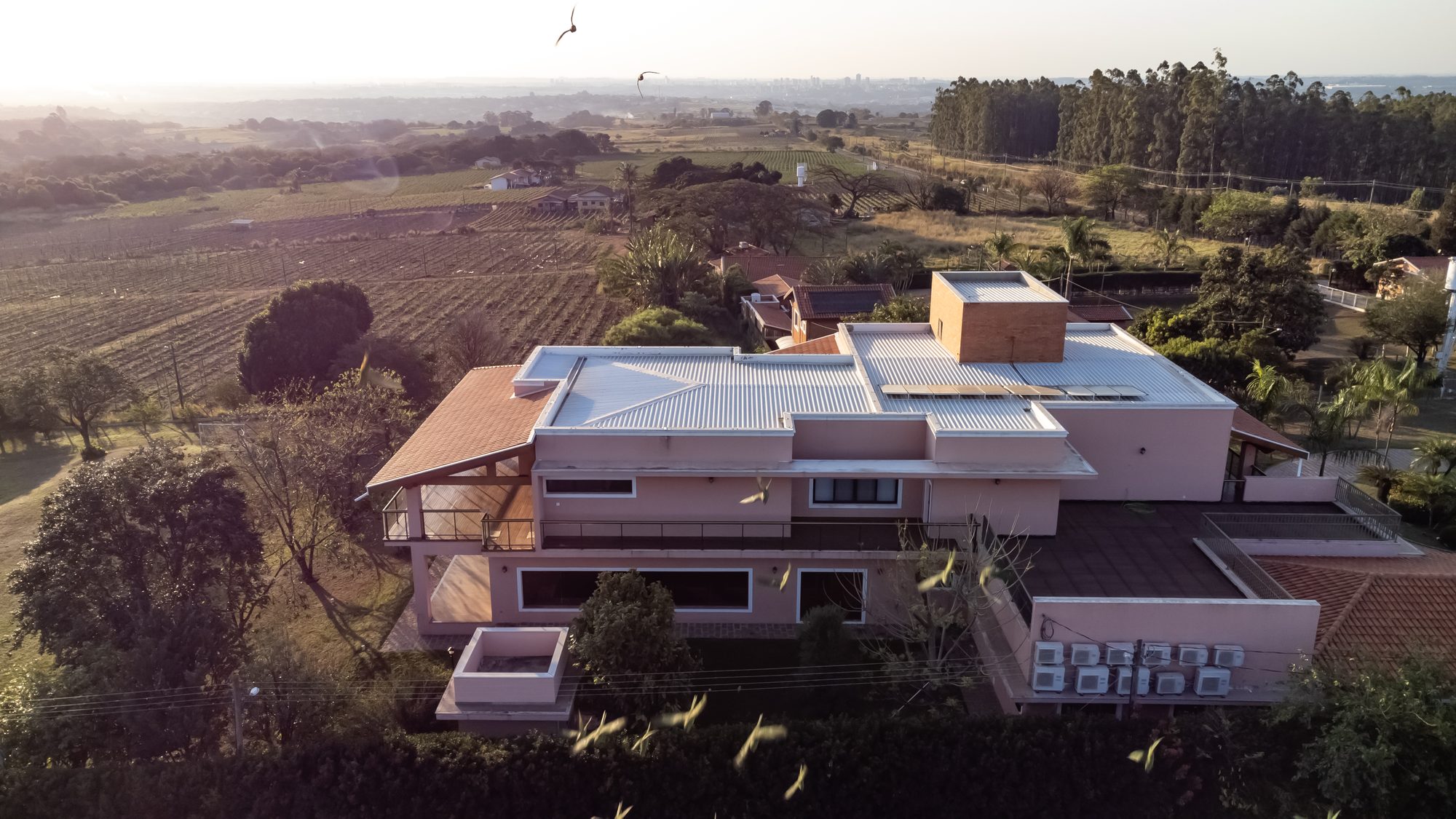 Vista aérea da Casa Cinema ao entardecer, cercada por área verde
