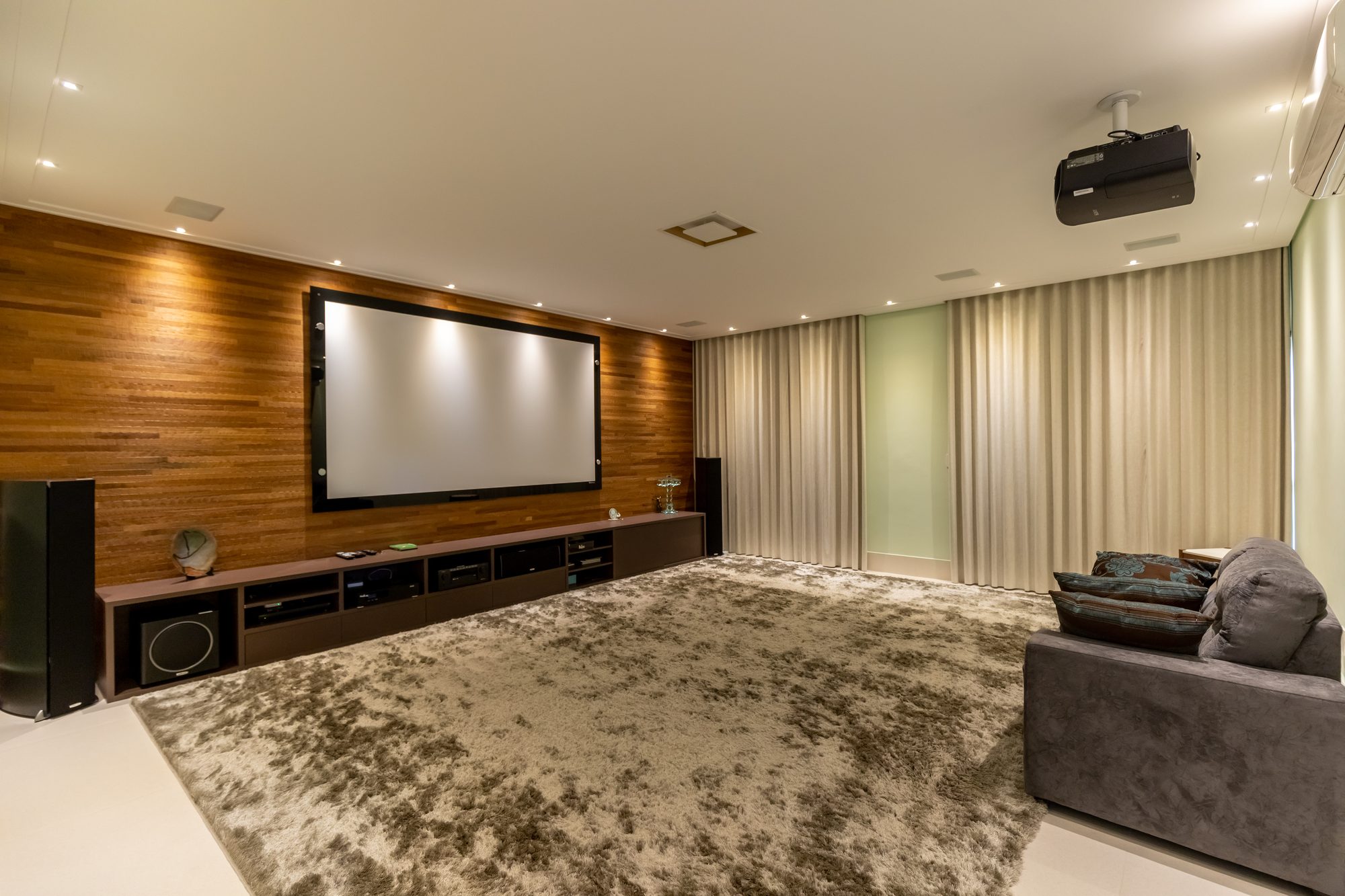 Sala de cinema com tela grande, painel de madeira e projetor 4K