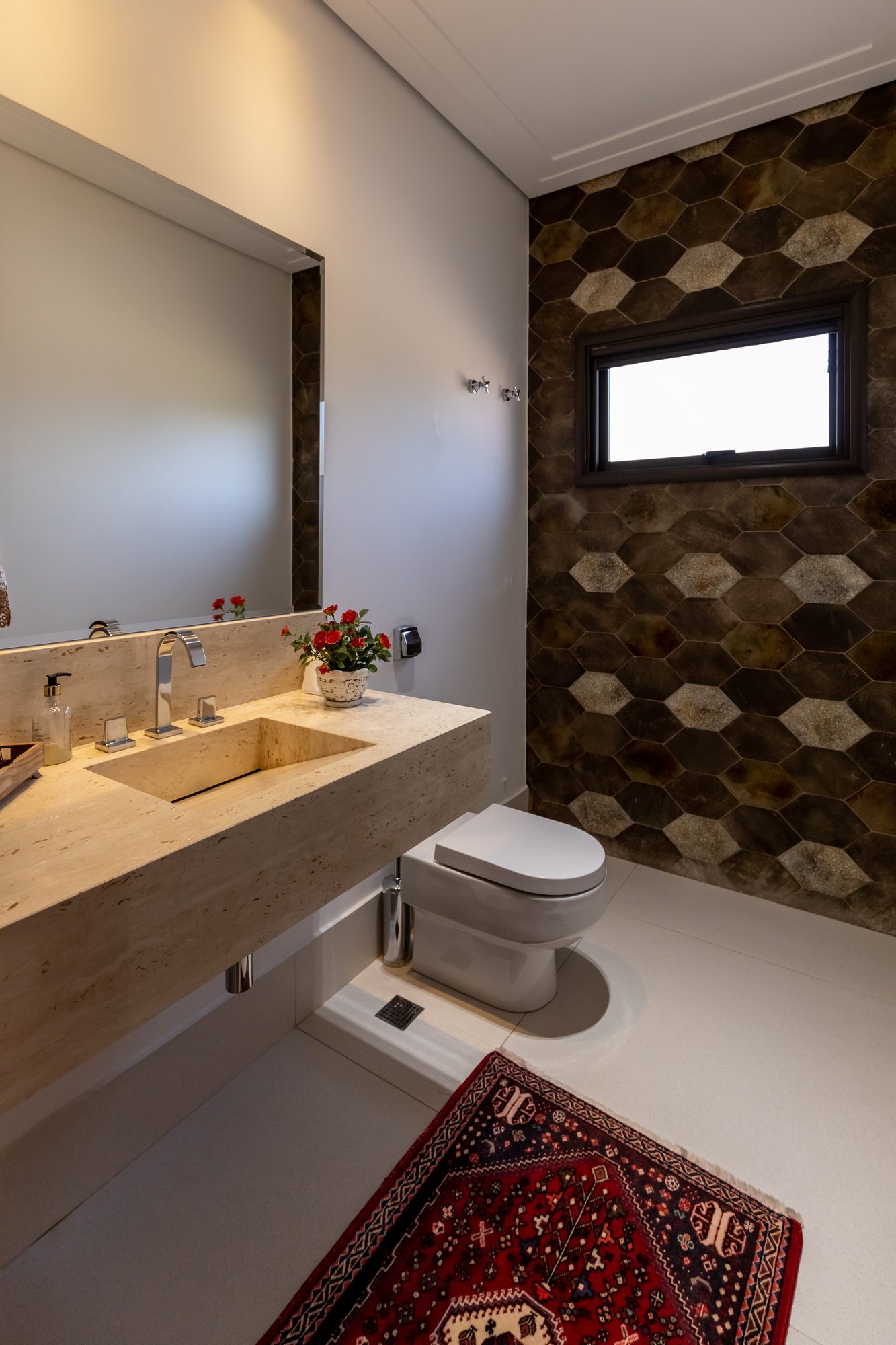 Lavabo com bancada de travertino e parede de azulejos hexagonais escuros