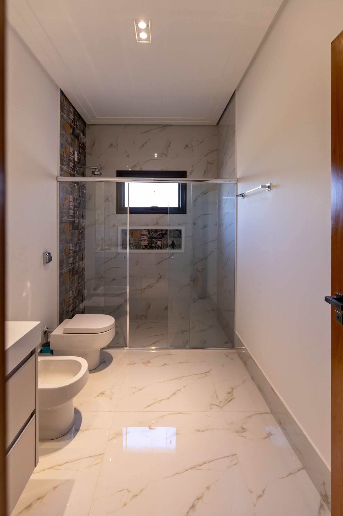 Banheiro em mármore branco com box de vidro e faixa decorativa