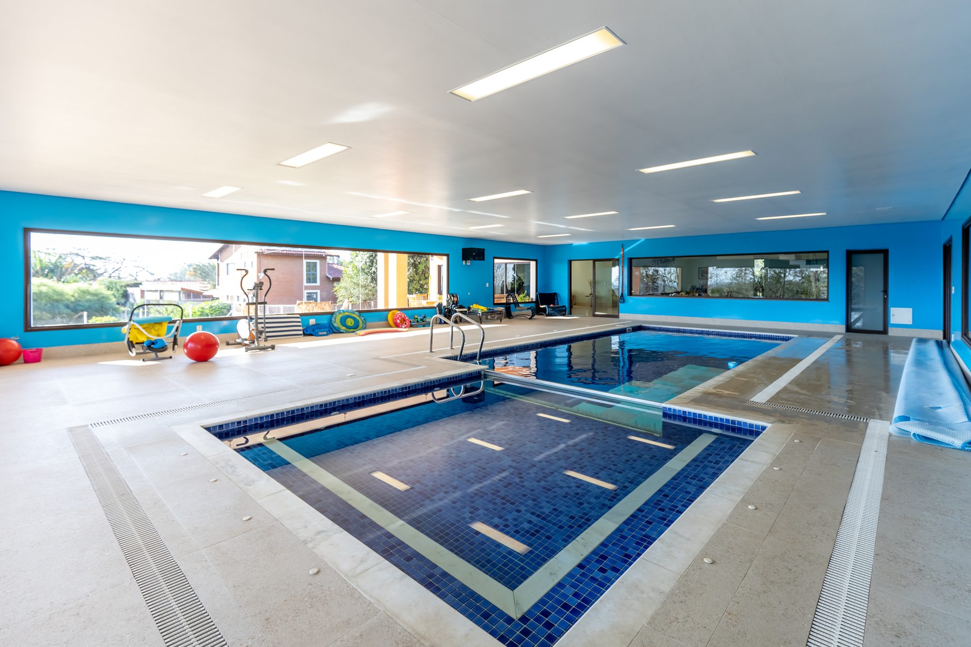 Piscina interna com prainha, aparelhos de ginástica e janelas amplas