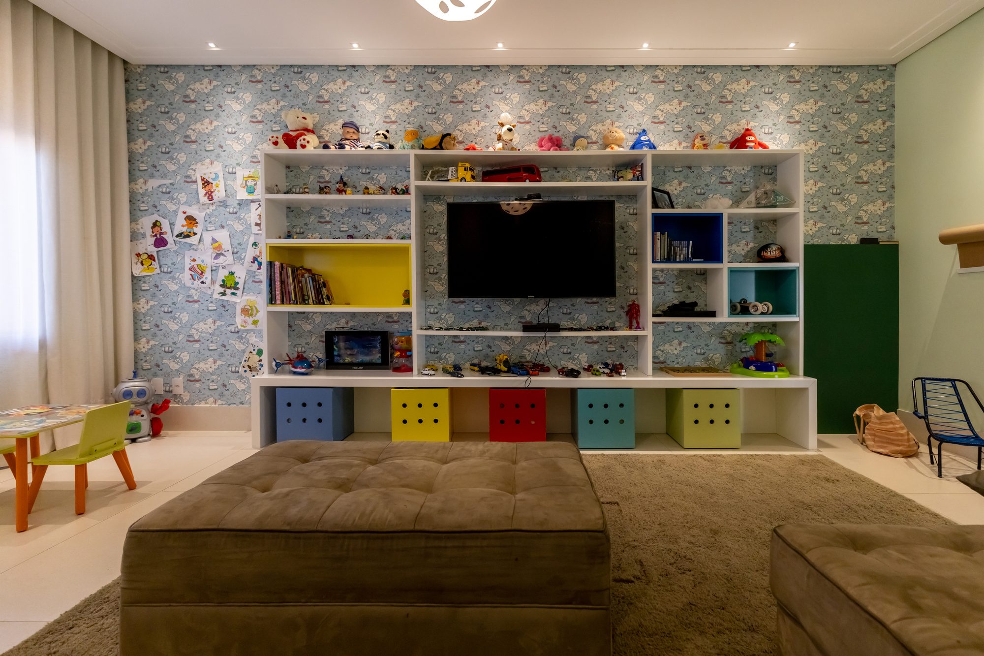 Painel da brinquedoteca com TV, livros, brinquedos e papel de parede de mapas