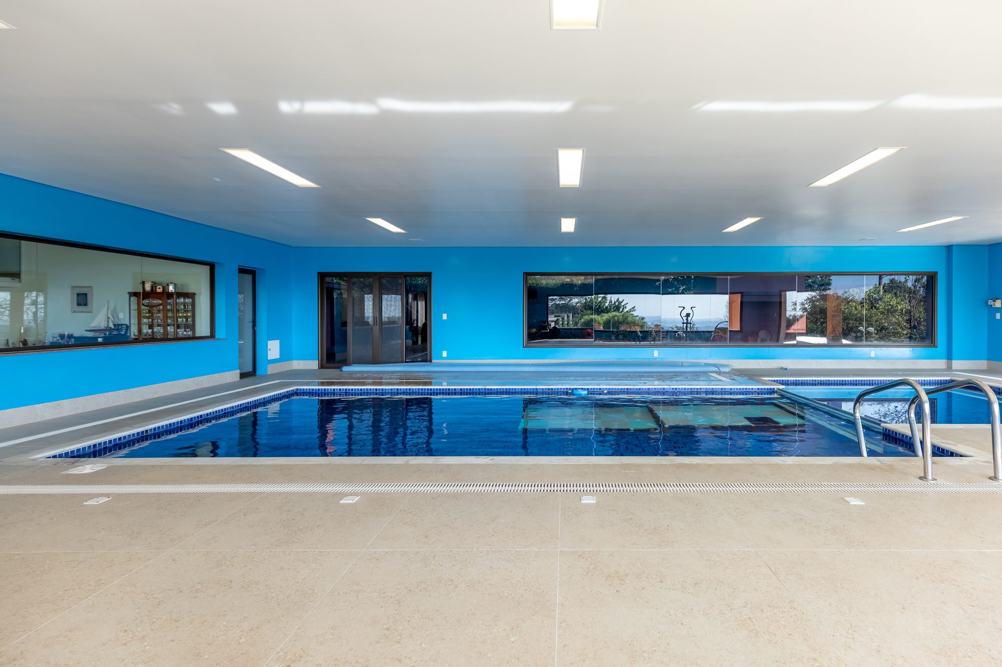 Piscina interna vista de frente, com janelões e iluminação embutida